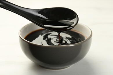 Photo of Taking soy sauce with spoon from bowl at white table, closeup