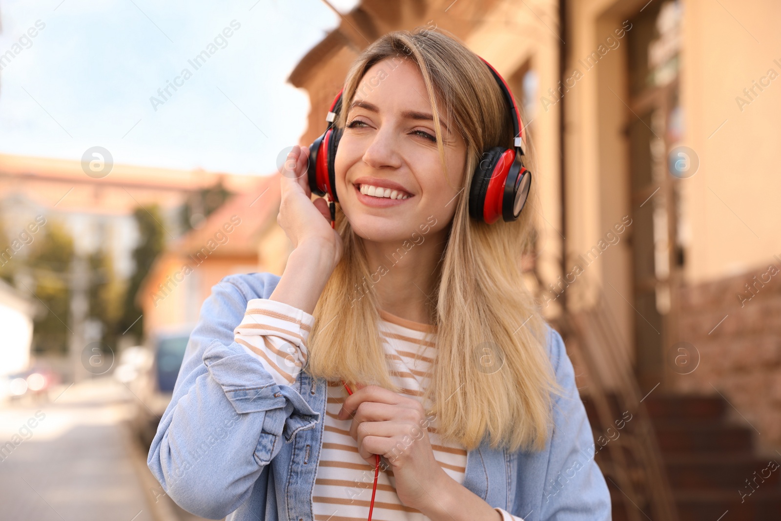 Photo of Happy young woman with headphones listening to music on city street