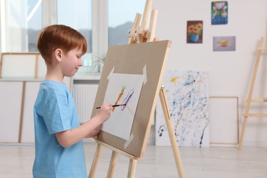 Photo of Little boy painting in studio. Using easel to hold canvas