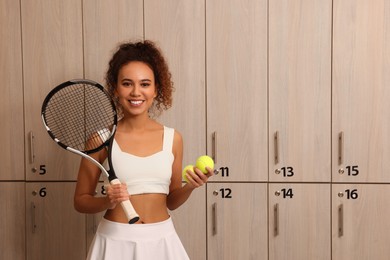 Photo of Beautiful young African American woman with tennis racket and balls in locker room