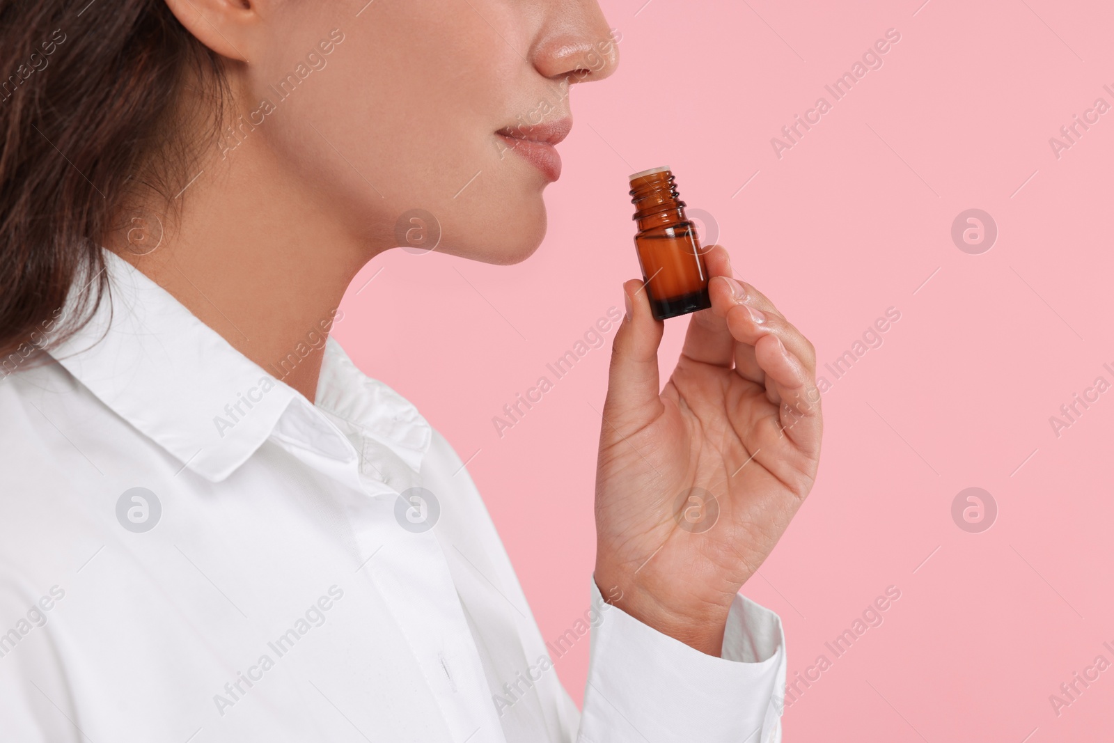 Photo of Woman with bottle of essential oil on pink background, closeup