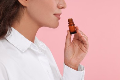 Photo of Woman with bottle of essential oil on pink background, closeup