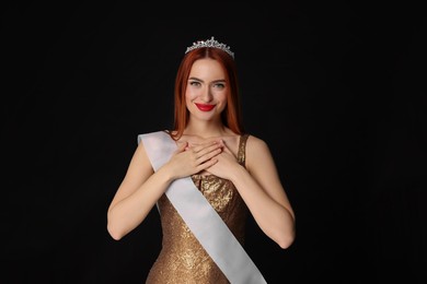 Photo of Beautiful young woman with tiara and ribbon in dress on black background. Beauty contest