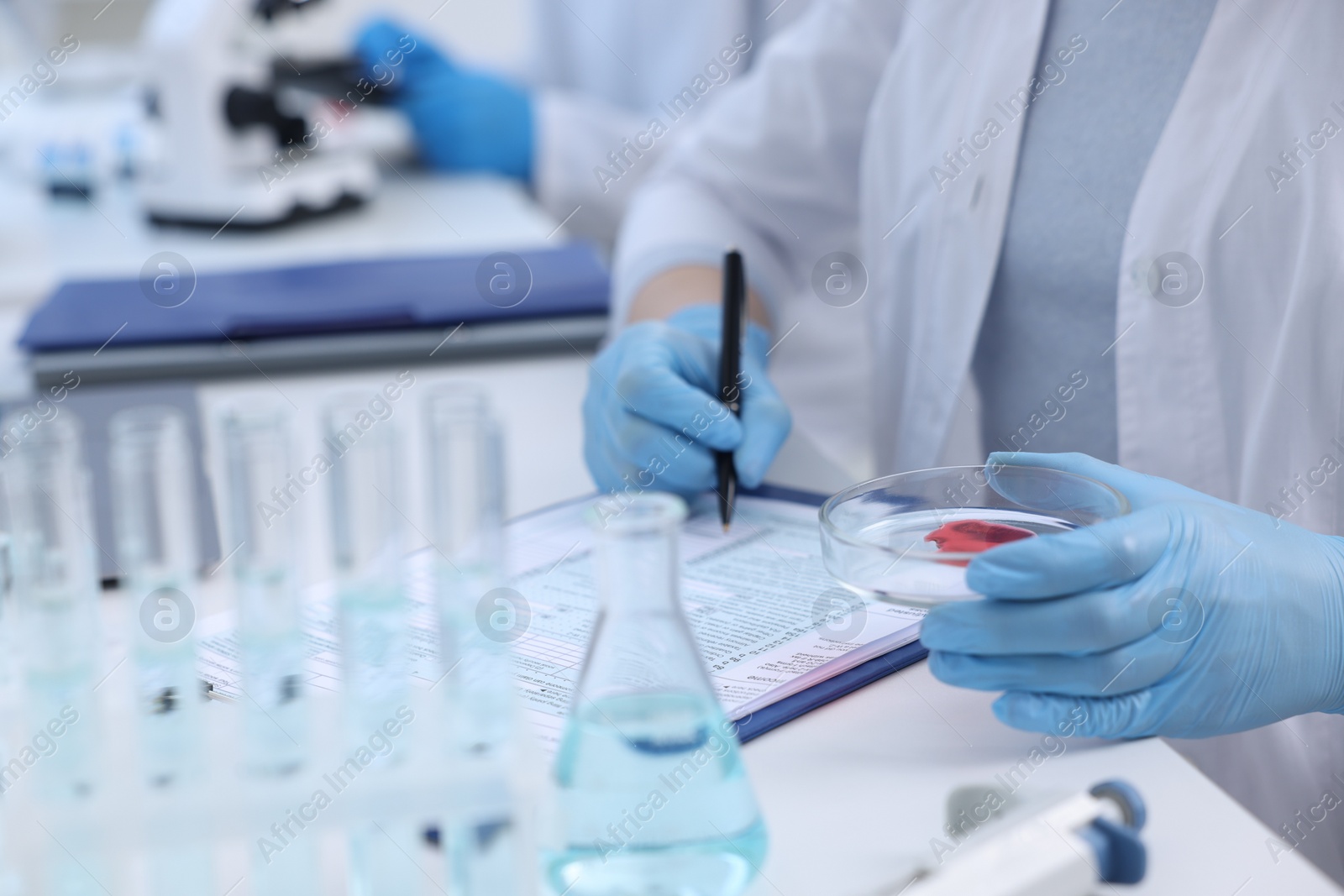 Photo of Laboratory worker holding petri dish with blood sample while working at white table, closeup