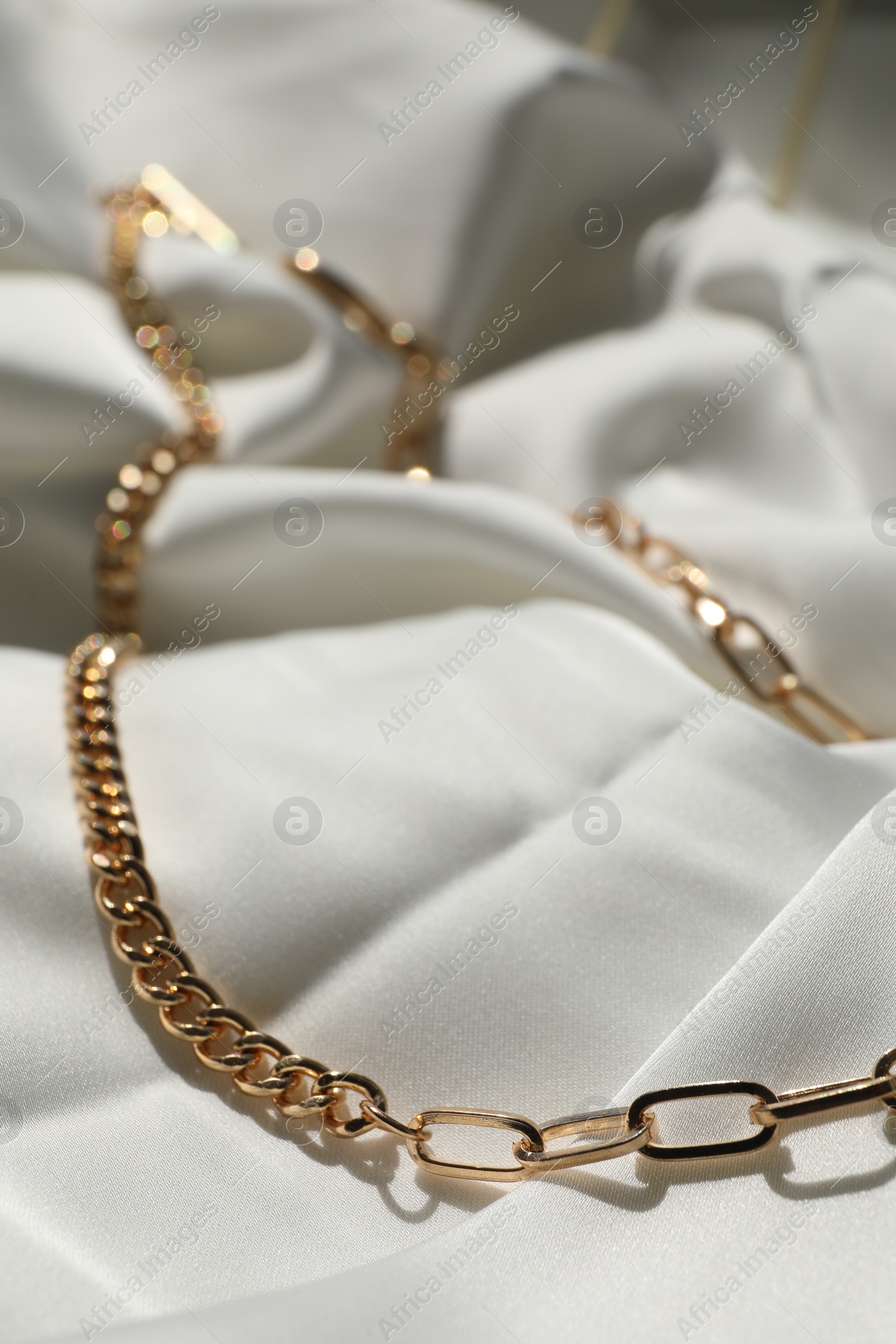 Photo of Metal chain on white fabric, closeup. Luxury jewelry