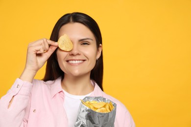 Beautiful woman holding potato chips near eye on orange background, space for text