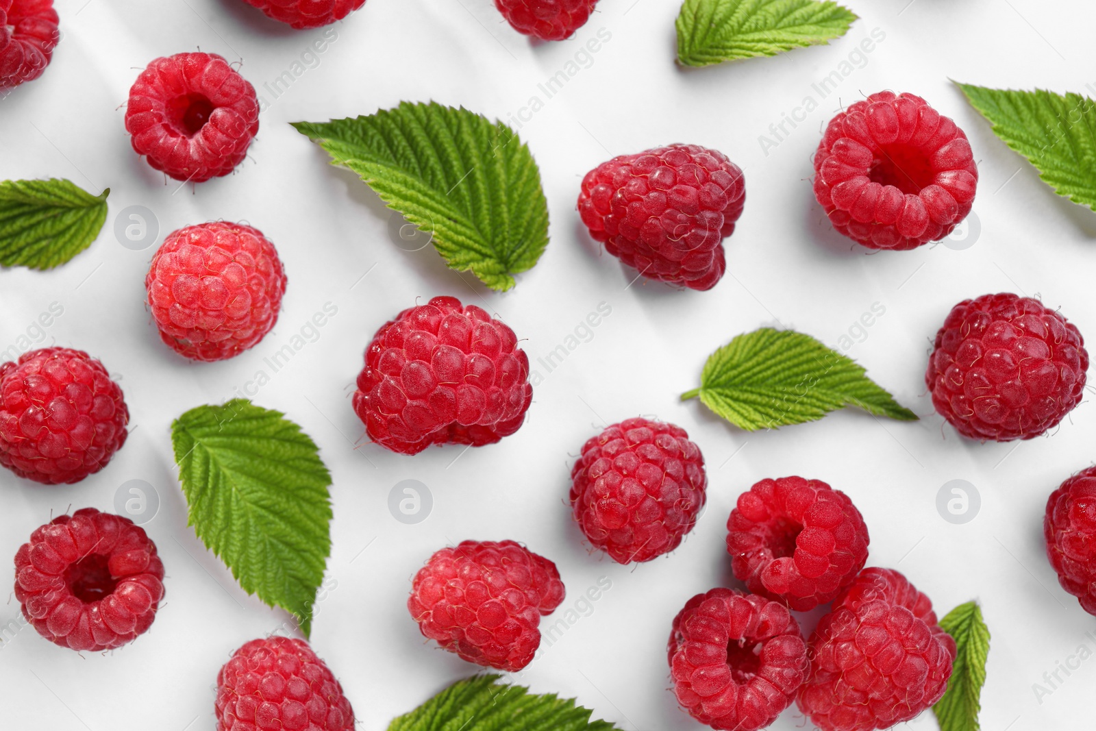 Photo of Tasty ripe raspberries and green leaves on white background, flat lay