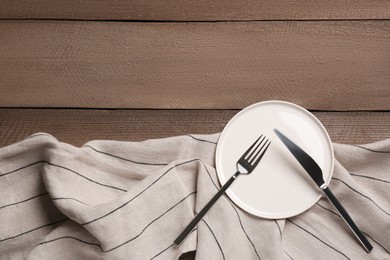 Clean plate and shiny silver cutlery on wooden table, flat lay. Space for text