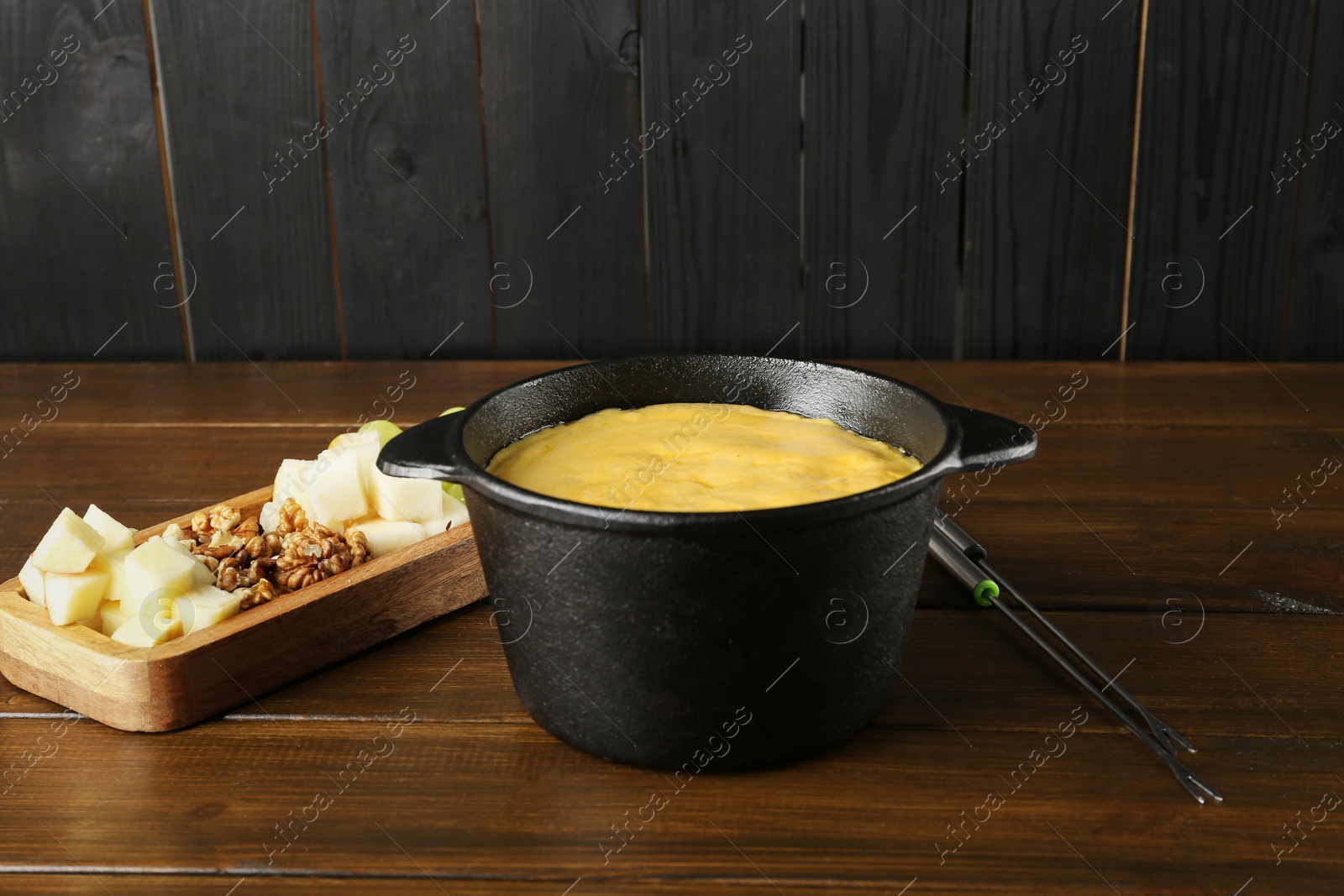 Photo of Fondue pot with melted cheese and different products on wooden table