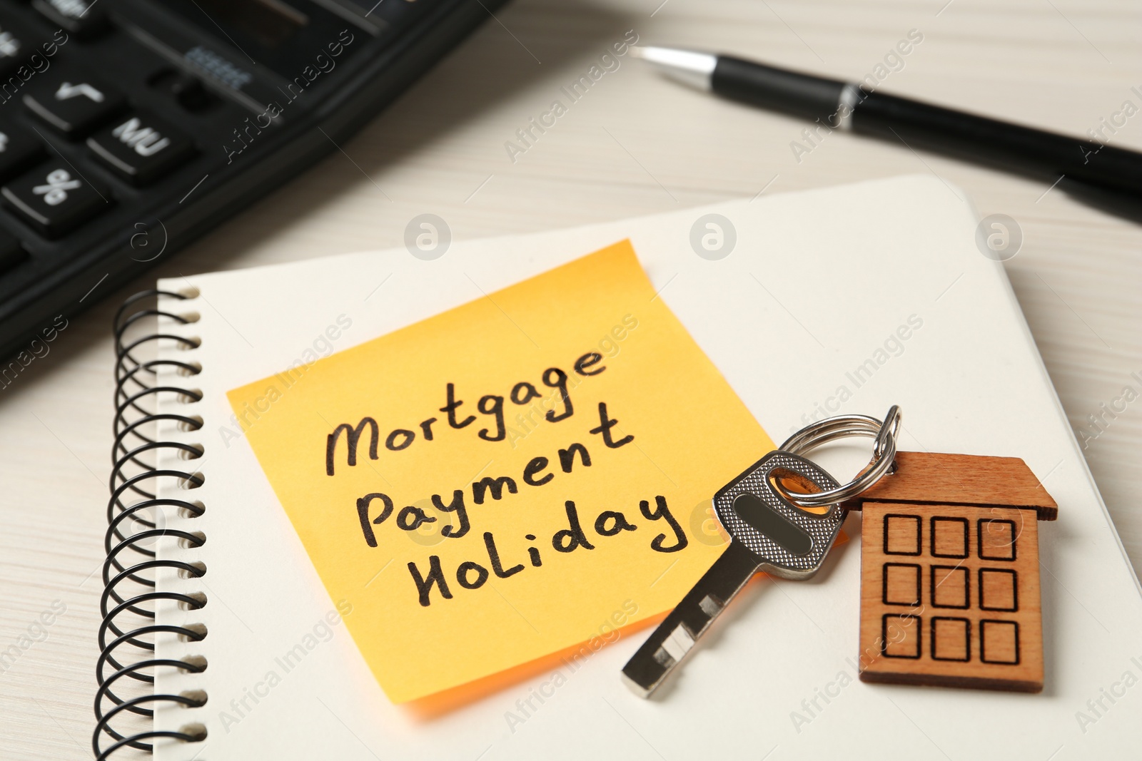 Photo of Paper note with words Mortgage Payment Holiday, key and notebook on white table, closeup