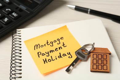 Photo of Paper note with words Mortgage Payment Holiday, key and notebook on white table, closeup
