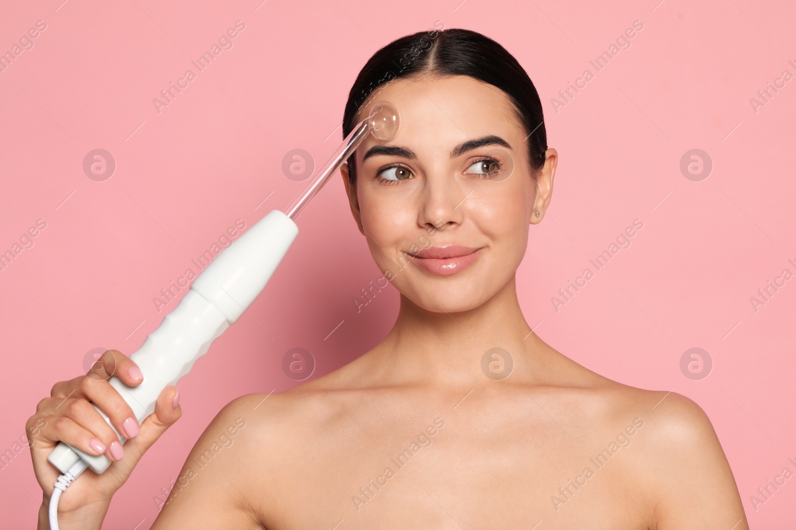 Photo of Woman using high frequency darsonval device on pink background. Space for text