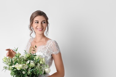 Photo of Young bride wearing wedding dress with beautiful bouquet on light background. Space for text