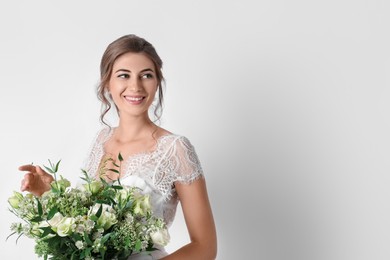 Young bride wearing wedding dress with beautiful bouquet on light background. Space for text