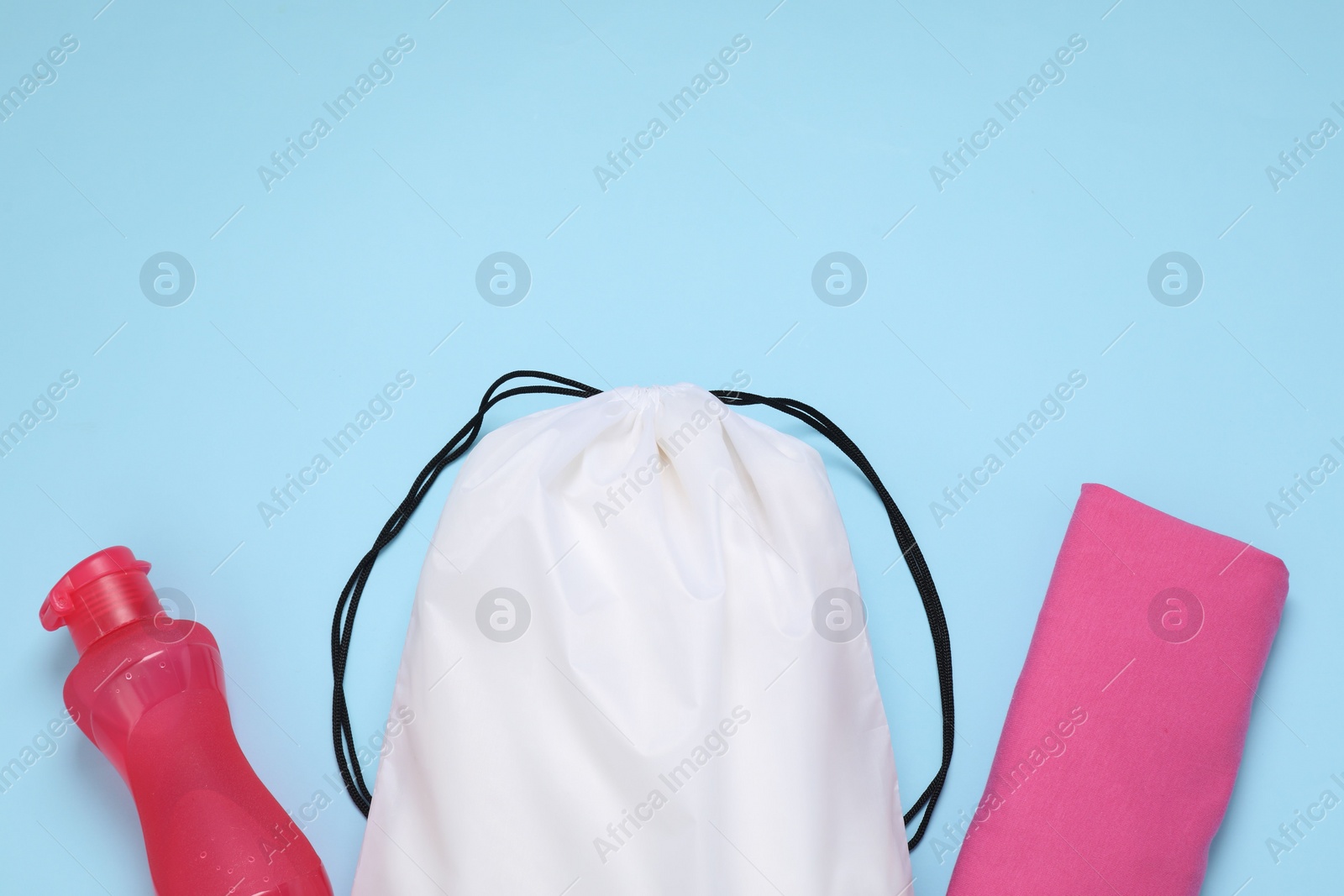 Photo of White drawstring bag, bottle and cloth on light blue background, flat lay. Space for text