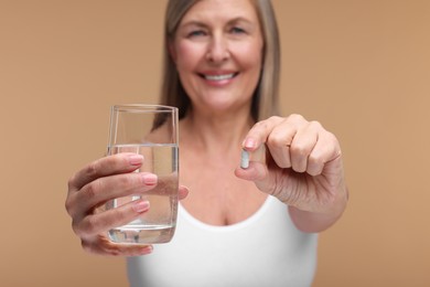 Photo of Beautiful woman with vitamin capsule and glass of water on beige background, selective focus