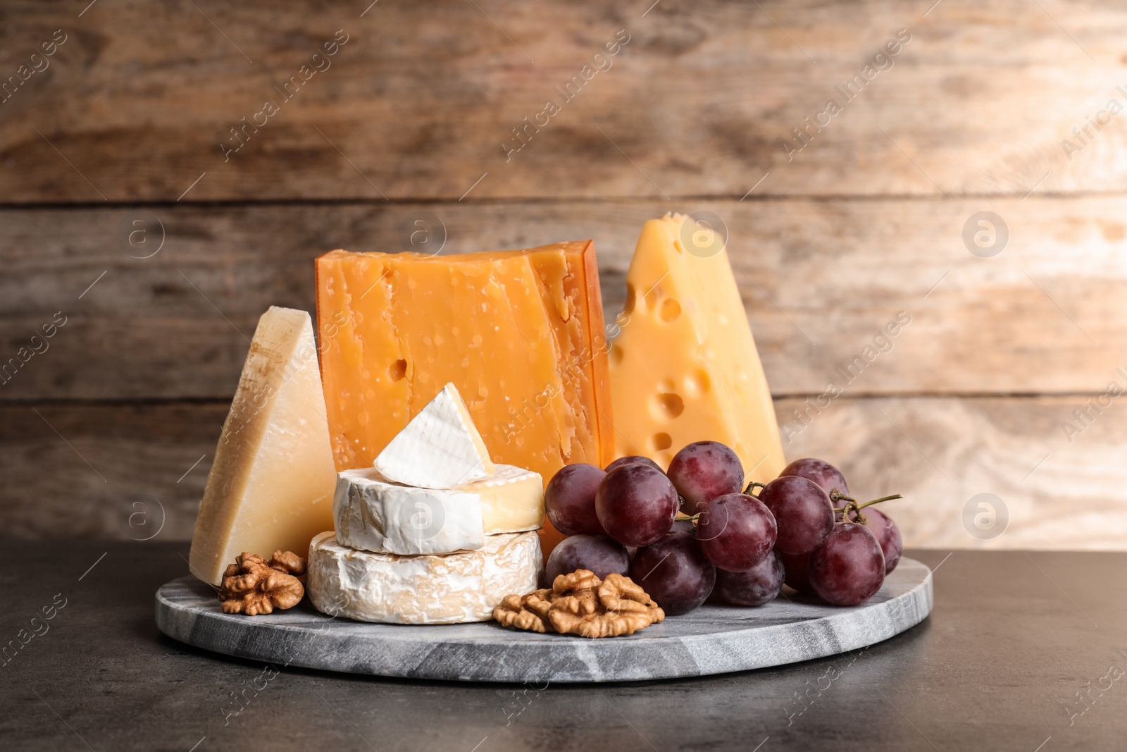 Photo of Composition with assorted cheese, grapes and walnuts on table against wooden background