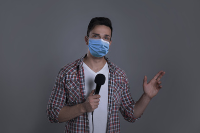 Young journalist with microphone wearing medical mask on grey background. Virus protection