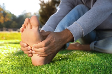 Photo of Man sitting barefoot on fresh green grass outdoors, closeup