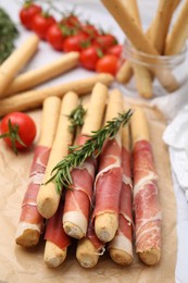 Photo of Delicious grissini sticks with prosciutto on white table