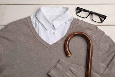 Elegant walking cane, sweater and glasses on white wooden table, flat lay