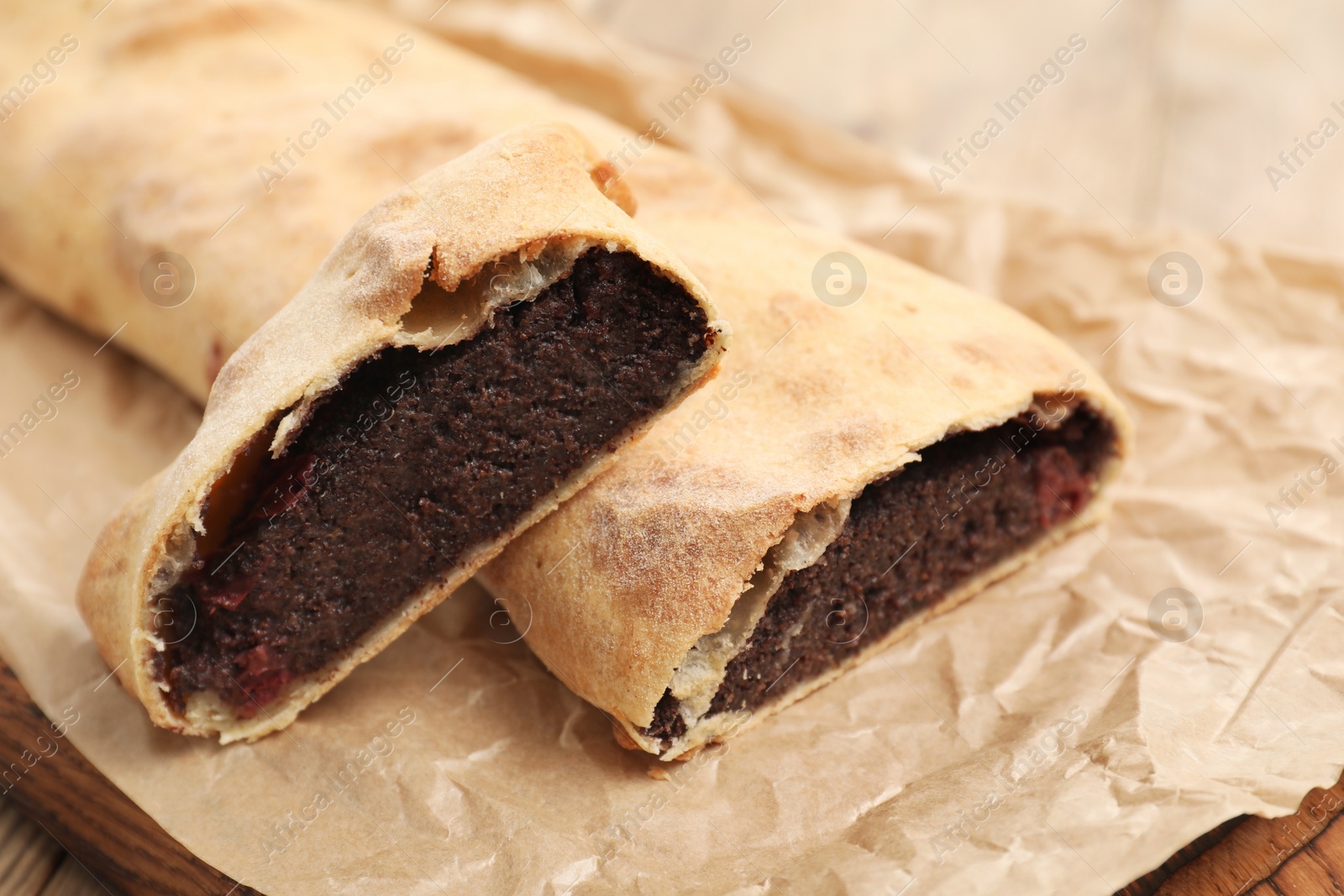 Photo of Delicious strudel with poppy seeds and cherries on parchment paper, closeup