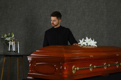 Photo of Sad young man near casket with white lilies in funeral home