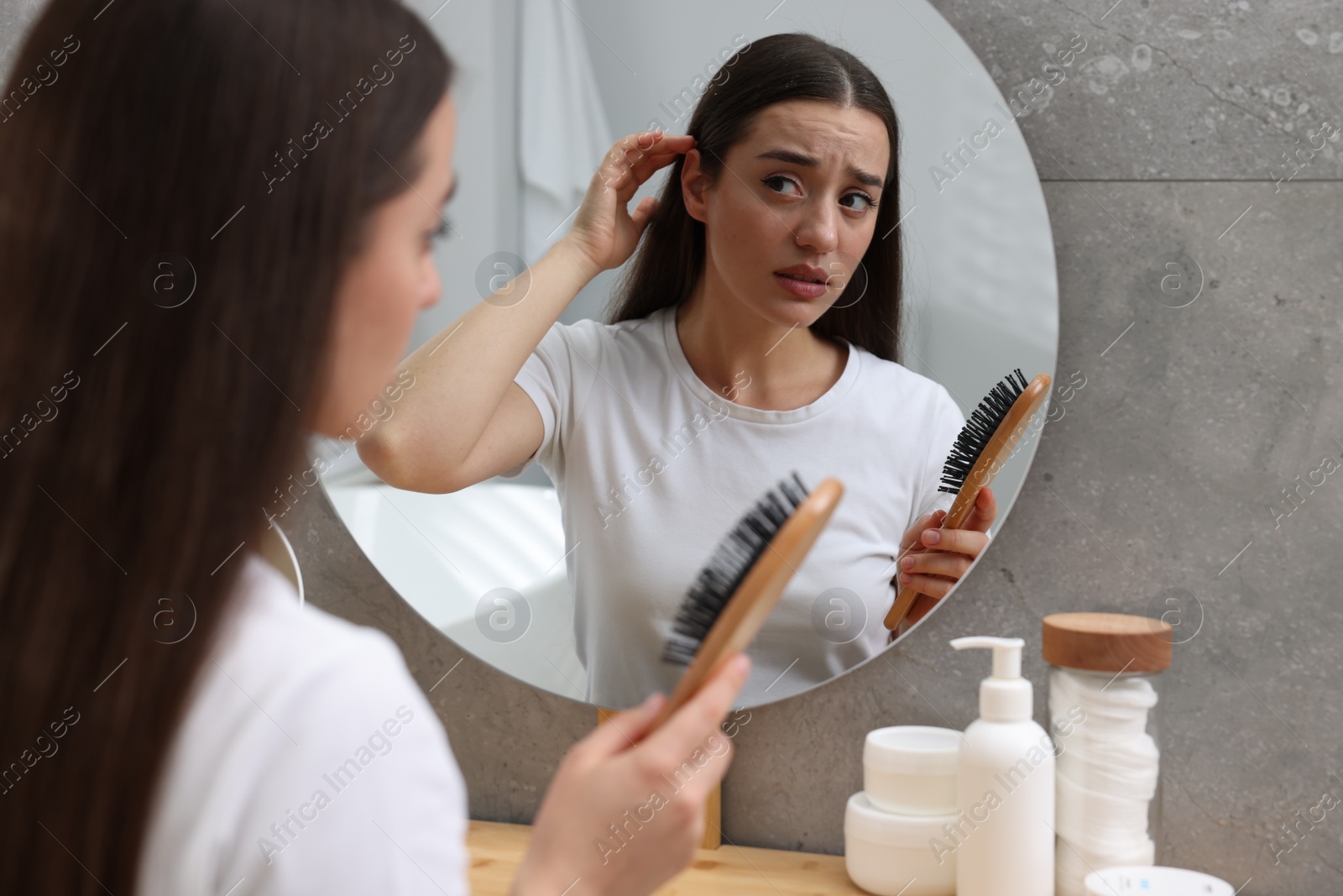 Photo of Emotional woman with brush suffering from dandruff near mirror at home.
