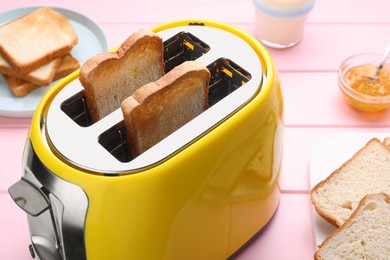 Photo of Yellow toaster with roasted bread and jam on pink wooden table, closeup
