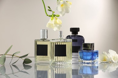 Photo of Luxury perfumes and floral decor on mirror surface against light grey background
