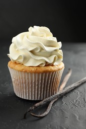 Photo of Tasty cupcake with cream and vanilla pods on black table, closeup