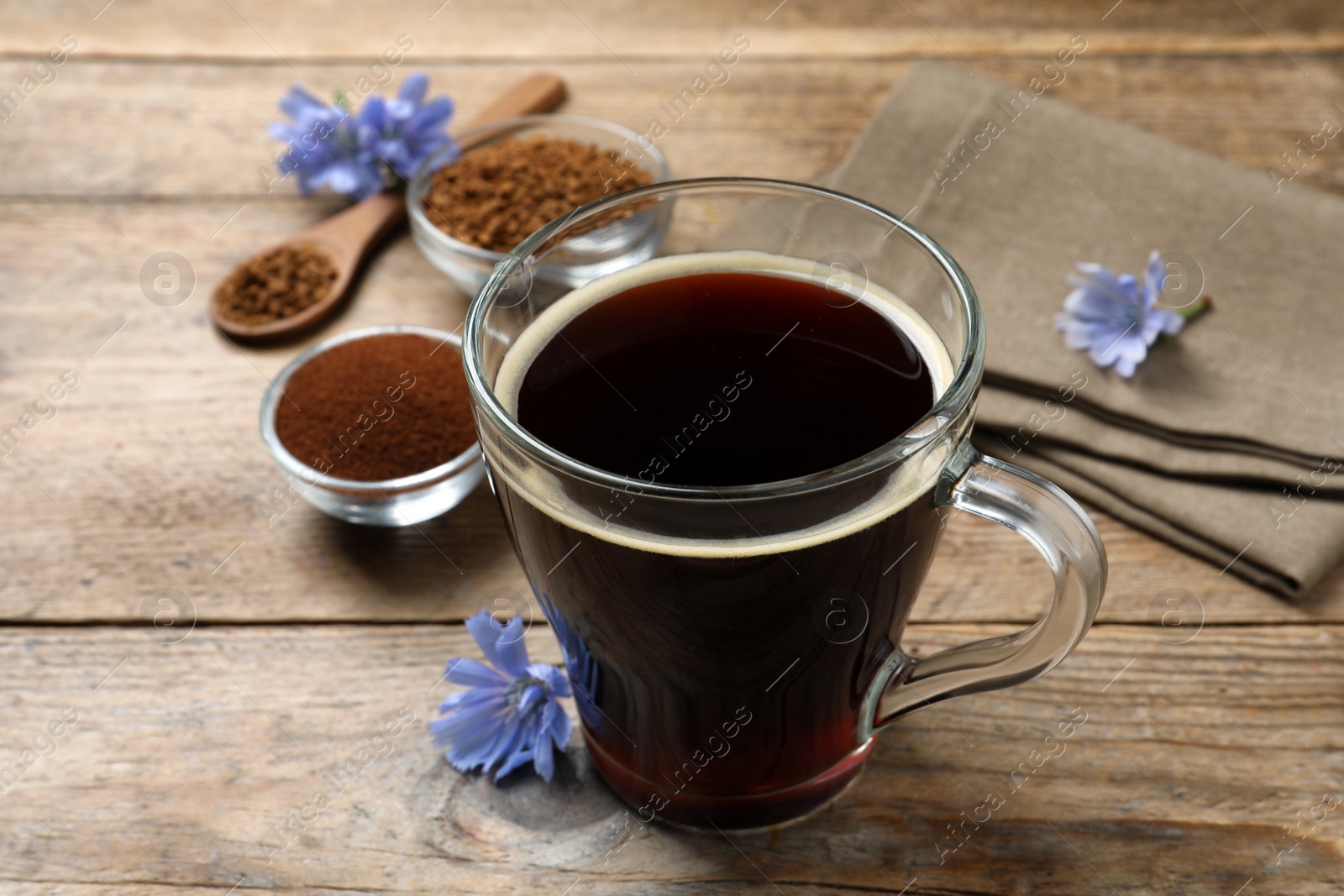 Photo of Glass cup of delicious chicory drink and flowers on wooden table, closeup