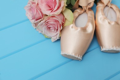 Photo of Beautiful beige ballet shoes and rose flowers on light blue wooden table. Space for text