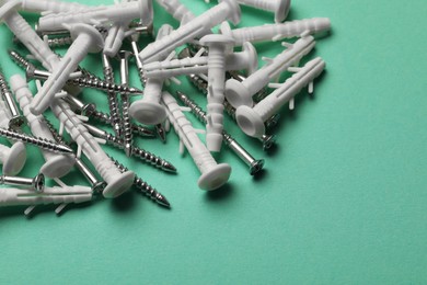 Many metal screws and white dowels on turquoise background, closeup