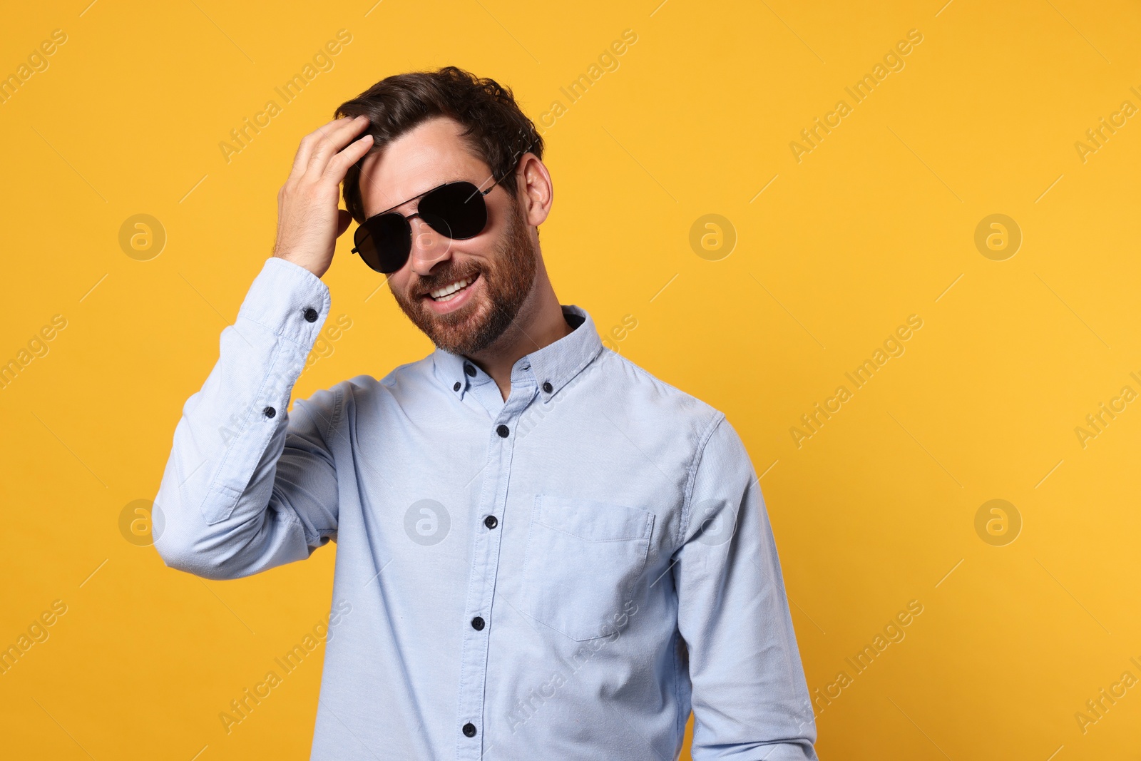 Photo of Portrait of smiling bearded man with stylish sunglasses on orange background. Space for text