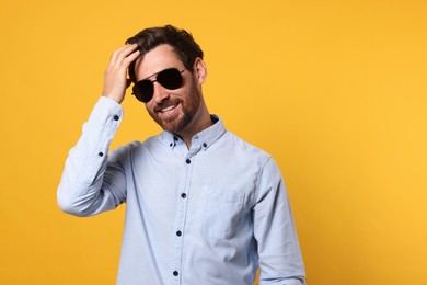 Photo of Portrait of smiling bearded man with stylish sunglasses on orange background. Space for text