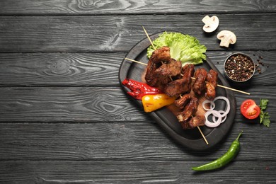 Delicious shish kebabs with vegetables and spices on black wooden table, flat lay. Space for text