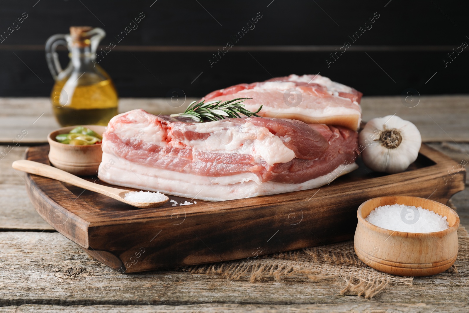 Photo of Pieces of raw pork belly, salt, oil, garlic and rosemary on wooden table