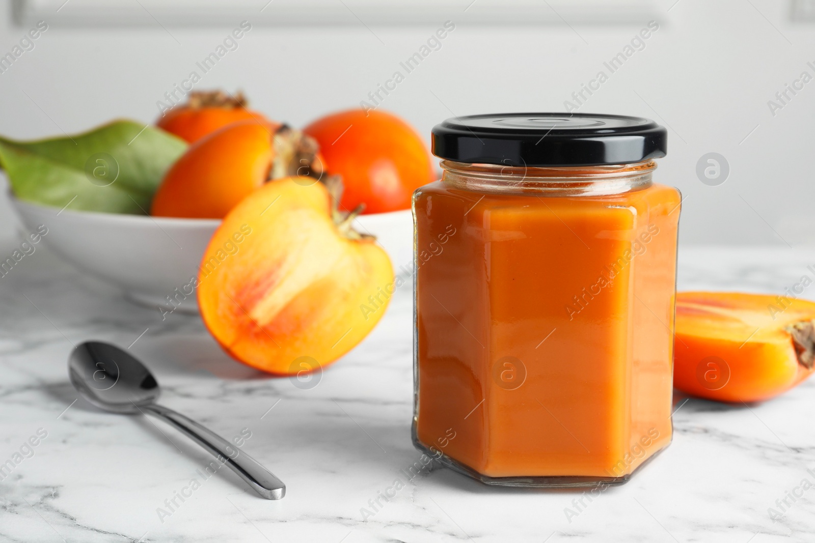 Photo of Delicious persimmon jam and fresh fruits on white marble table