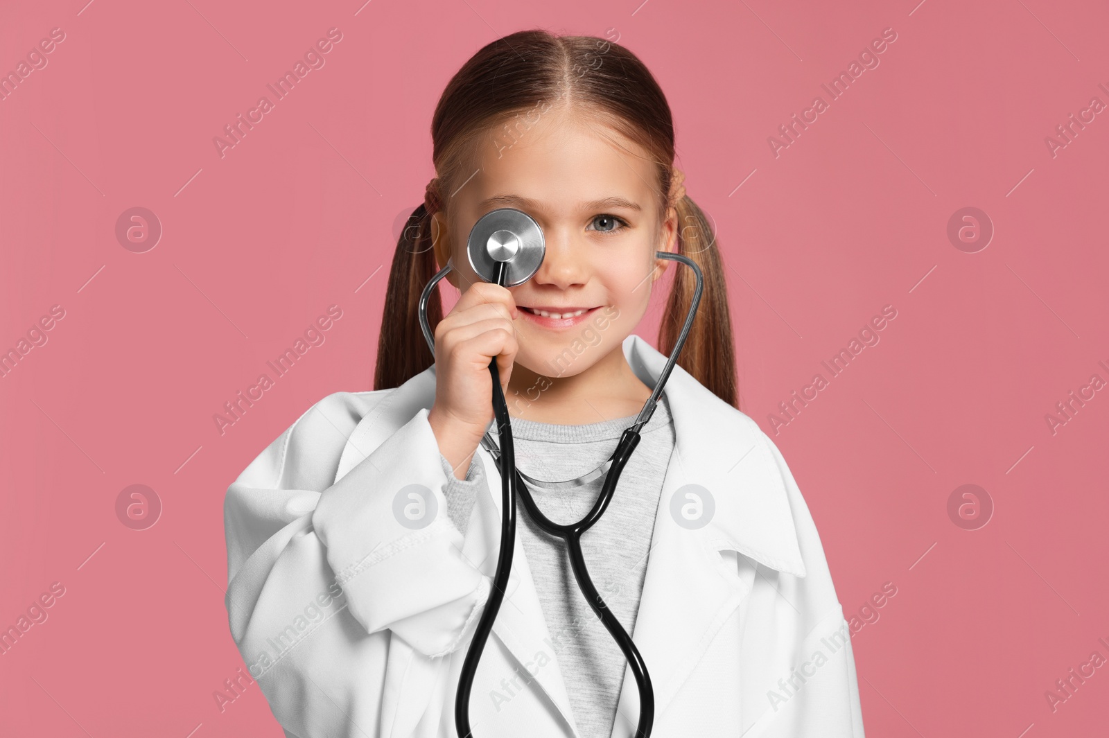 Photo of Little girl in medical uniform with stethoscope on pink background