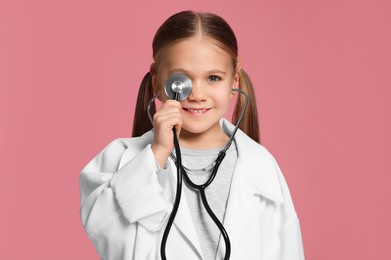 Photo of Little girl in medical uniform with stethoscope on pink background