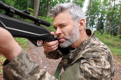 Photo of Man wearing camouflage and aiming with hunting rifle in forest