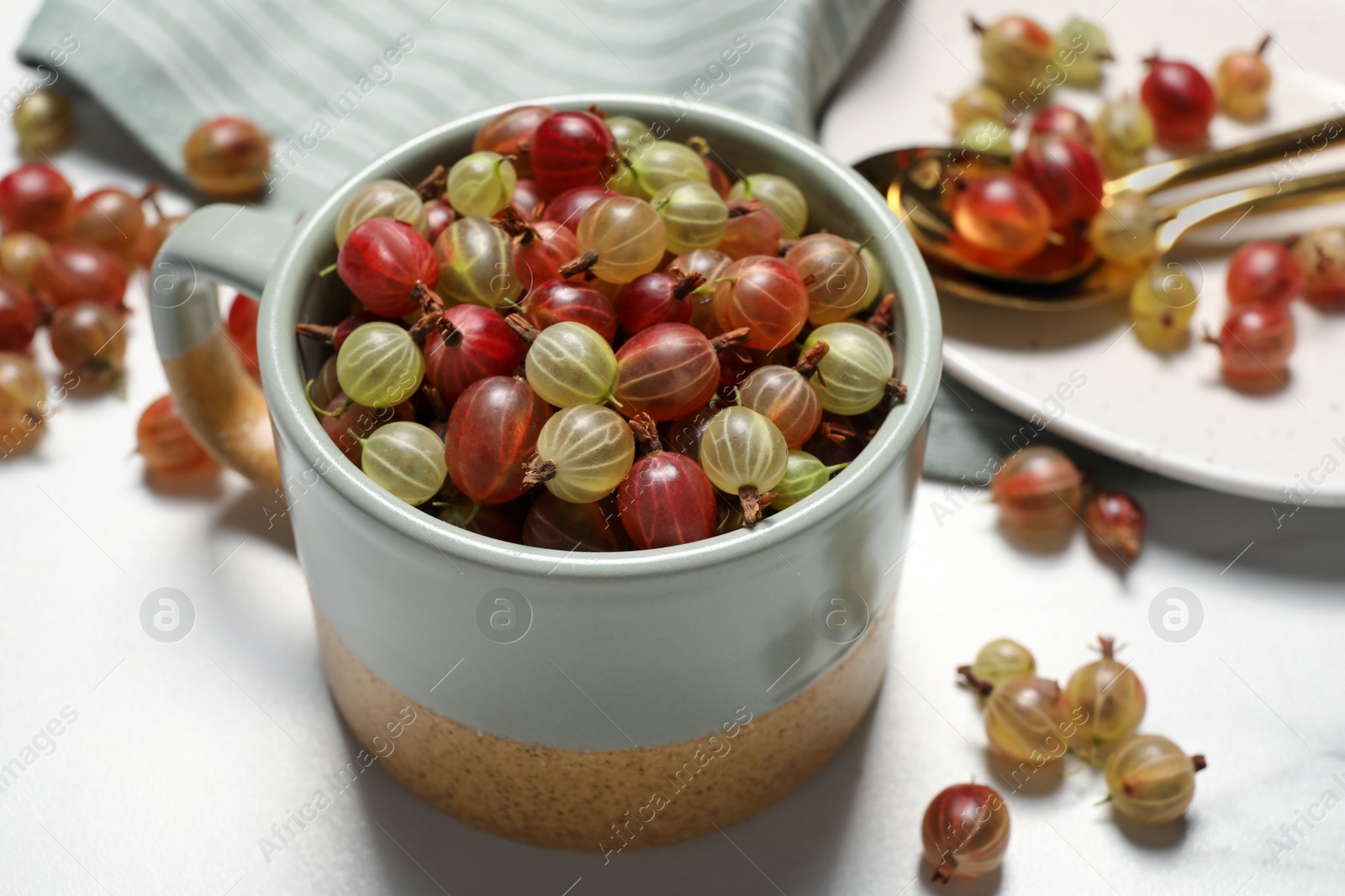 Photo of Cup with fresh ripe gooseberries on white table, closeup