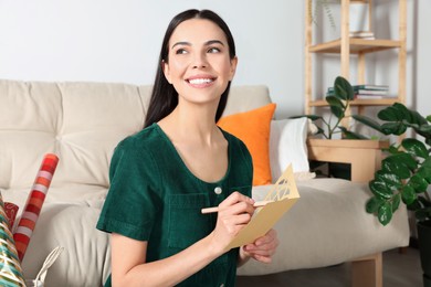 Photo of Happy woman writing message in greeting card on floor in living room