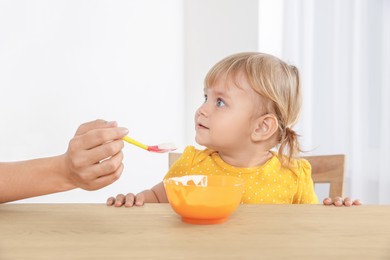 Mother feeding her cute little child with yogurt at wooden table indoors