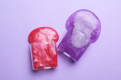 Photo of Overturned plastic containers with bright slimes on violet background, top view