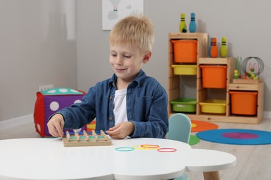 Photo of Motor skills development. Boy playing with geoboard and rubber bands at white table in room