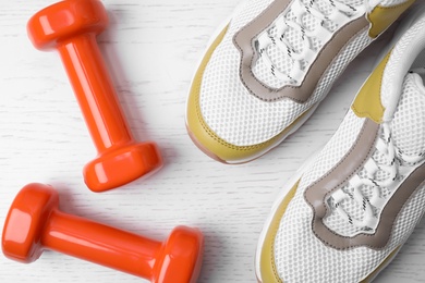 Photo of Dumbbells and sneakers on wooden background, flat lay