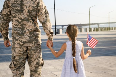 Photo of Soldier and his little daughter with American flag outdoors, back view. Veterans Day in USA