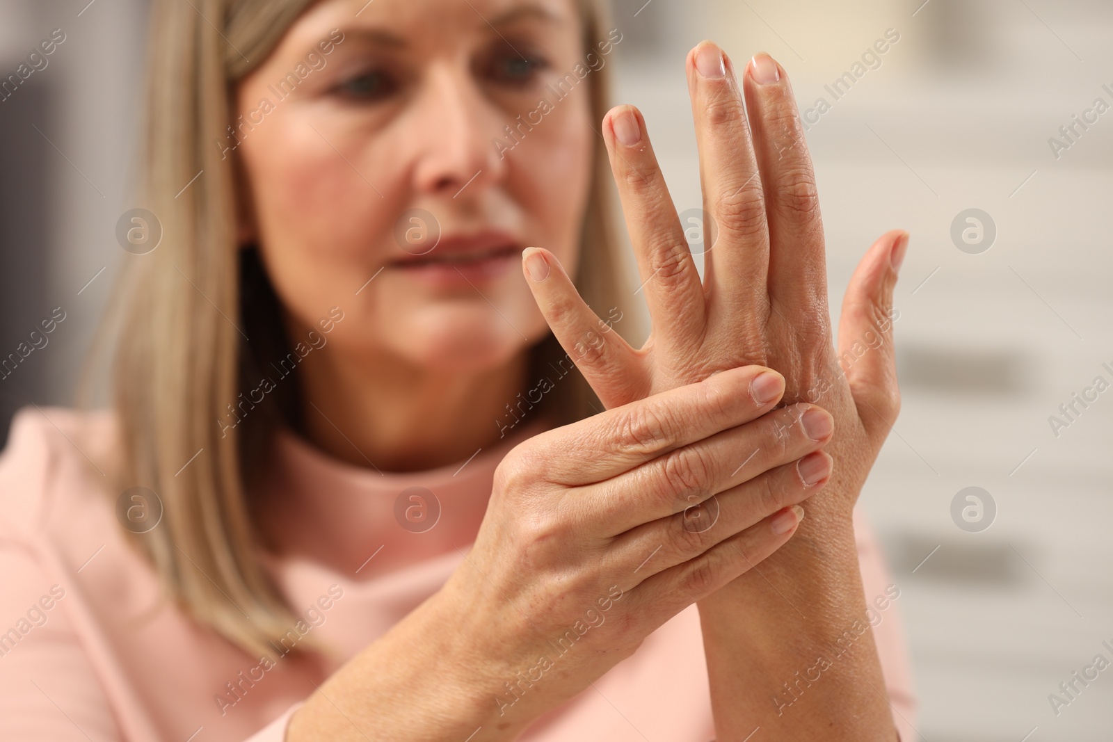 Photo of Mature woman suffering from pain in hand on blurred background, selective focus. Rheumatism symptom